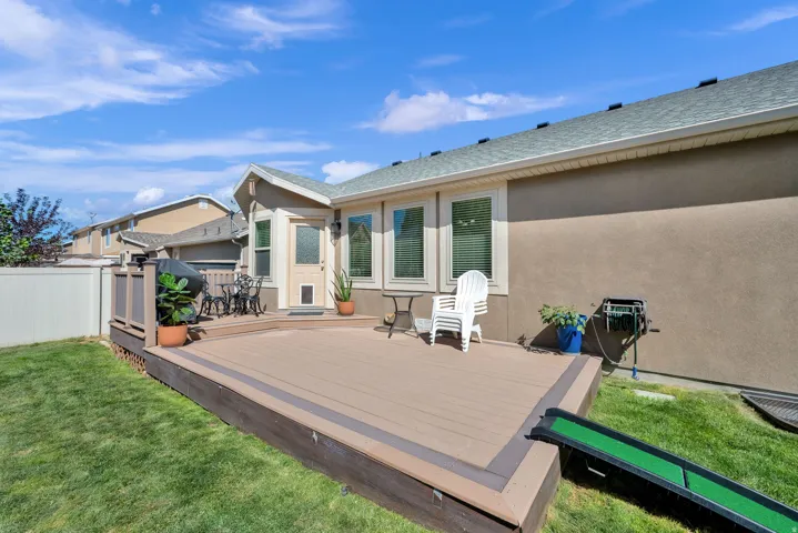 Expansive wood-finish deck with integrated railing, exterior wall with multiple windows, and a landscaped lawn