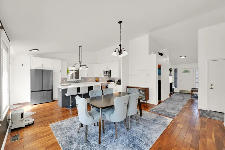 Open-concept interior featuring wood-finish flooring, white walls, and a kitchen with white cabinetry, a central island, and stainless steel appliances