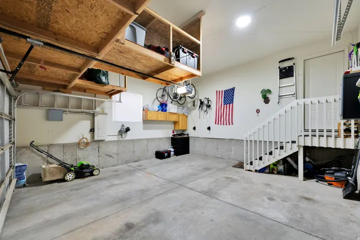 Concrete floor garage with built-in overhead shelving, a built-in workbench, and a white painted stairway