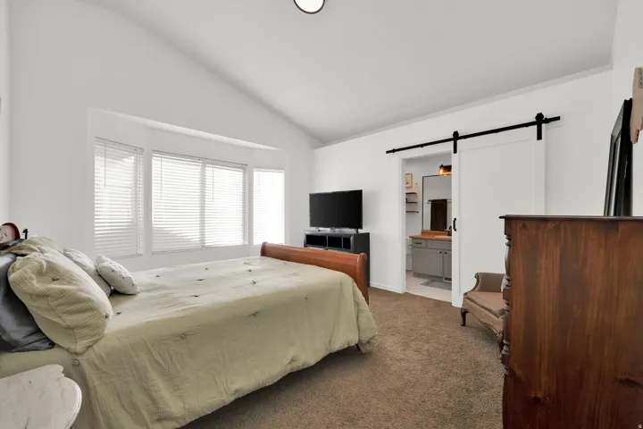 Vaulted ceiling, bay window, sliding barn door, bathroom vanity with integrated sink, and recessed lighting