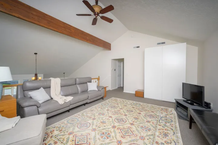 Vaulted ceiling with wood-finish beam, ceiling fan, and carpeted flooring