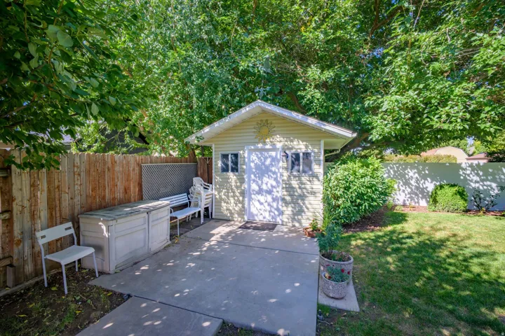 Detached storage shed with siding exterior, concrete patio, and fenced perimeter