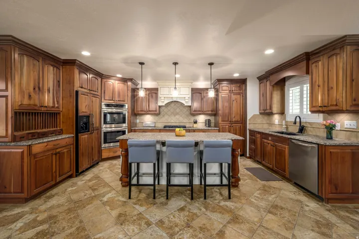 Kitchen featuring wood cabinetry, granite countertops, tile flooring, stainless steel appliances, and a central island with pendant lighting