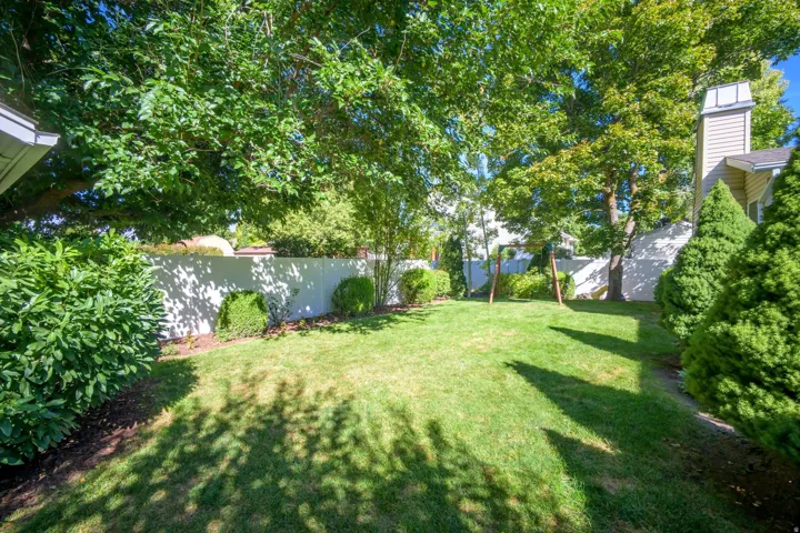Expansive backyard featuring a manicured lawn, established perimeter landscaping, and a privacy fence