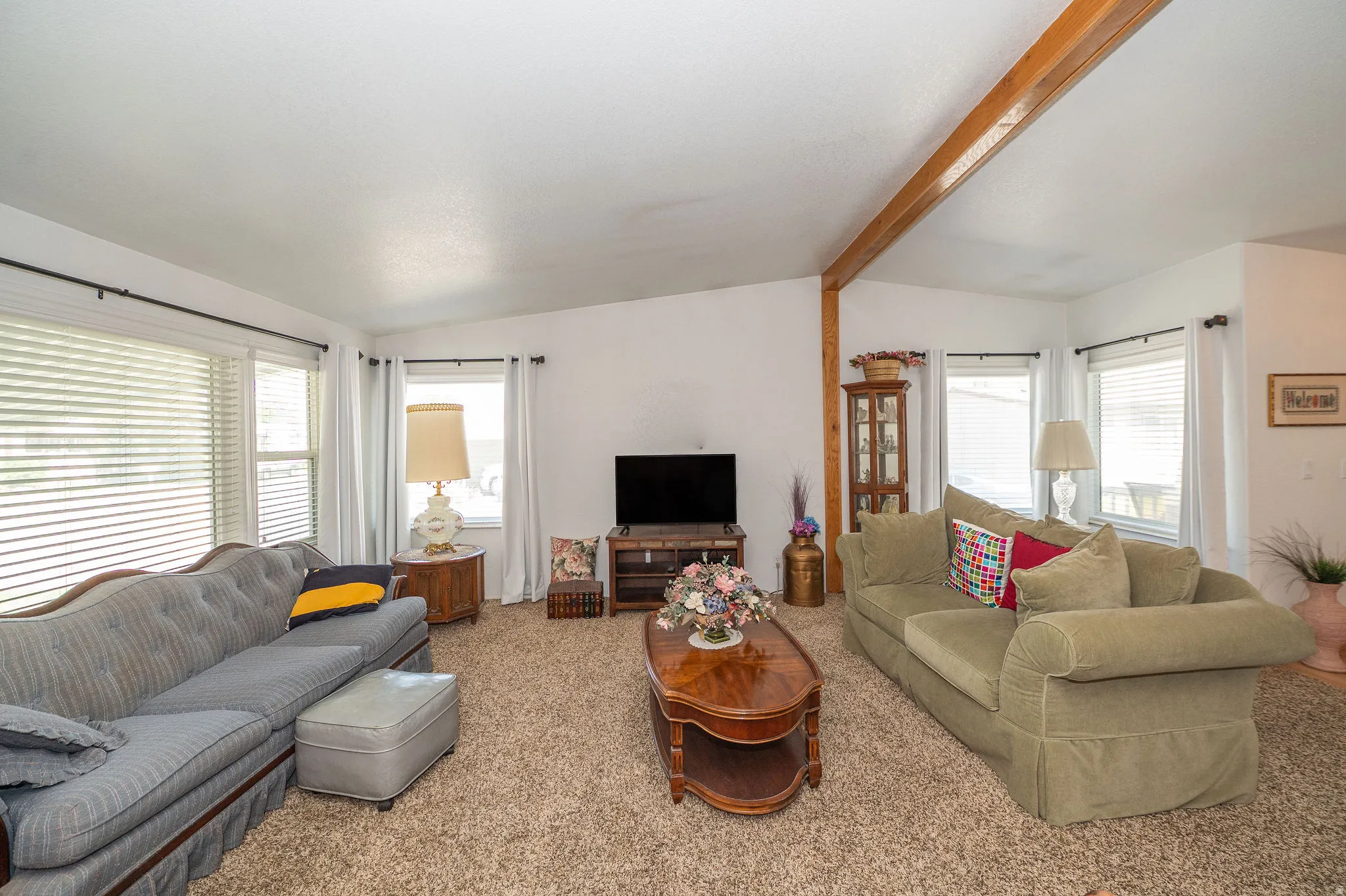 Vaulted ceiling with an exposed wood beam, multiple windows with blinds, and carpeted flooring