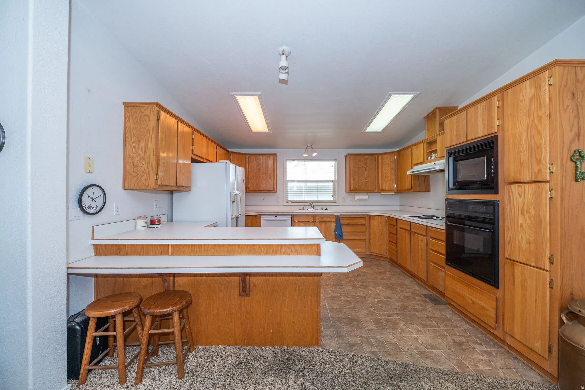 Spacious kitchen featuring extensive wood cabinetry, white laminate countertops, a built-in oven and microwave, and a breakfast bar