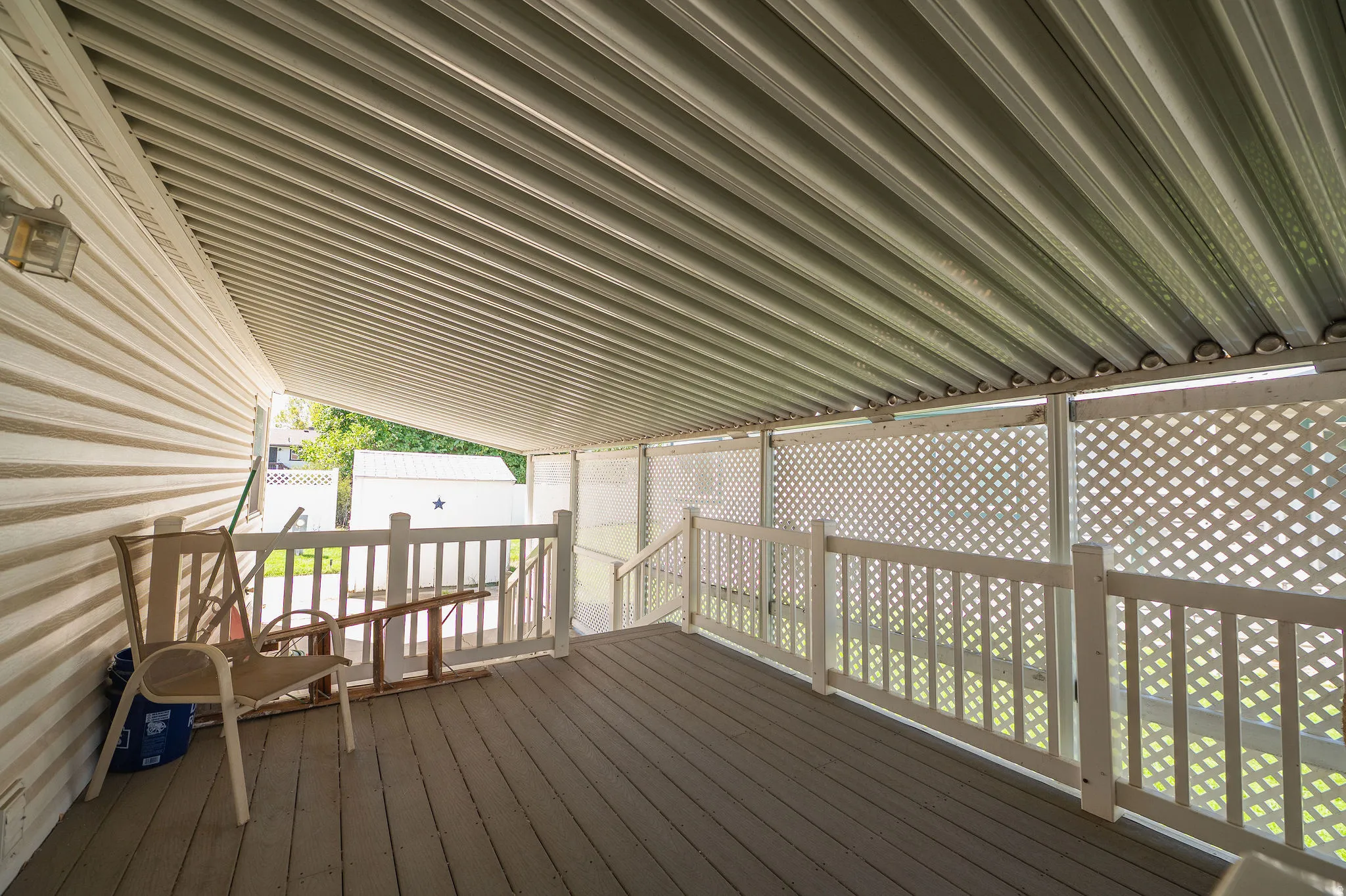 Covered deck featuring finish flooring, white lattice panels, white railing, and exterior wall siding
