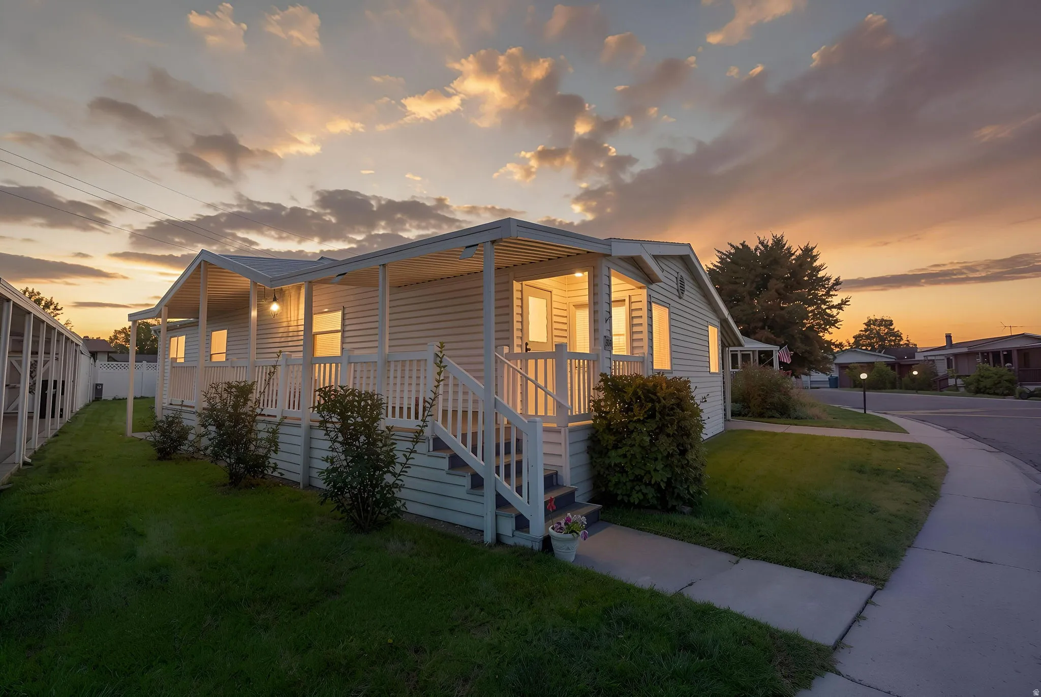 Covered front porch, white siding exterior, paved sidewalk, grass lawn, and established shrubbery