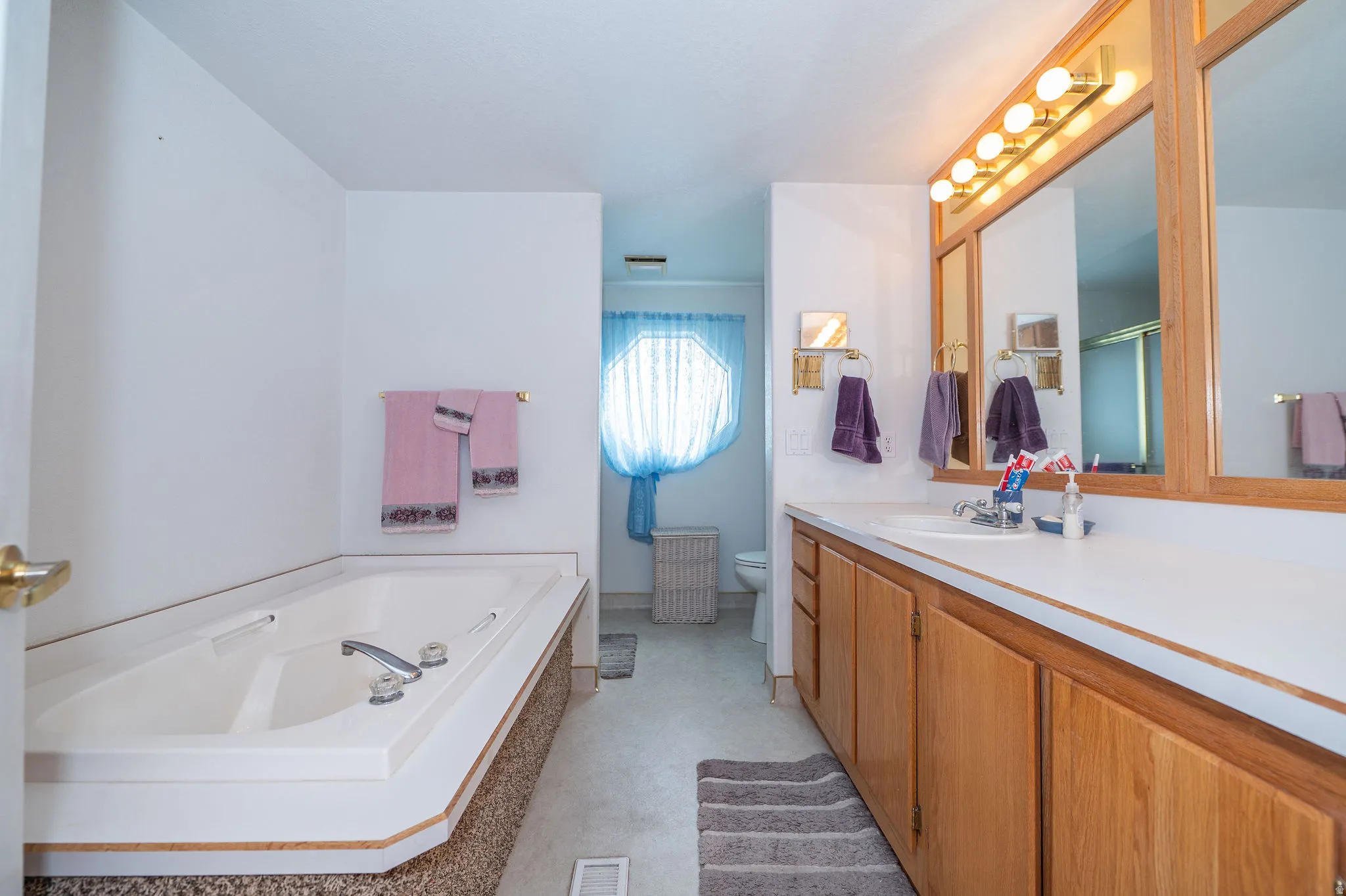 Built-in soaking tub, expansive vanity with integrated sink, wood-finish cabinetry, triple framed mirrors, and overhead vanity lighting