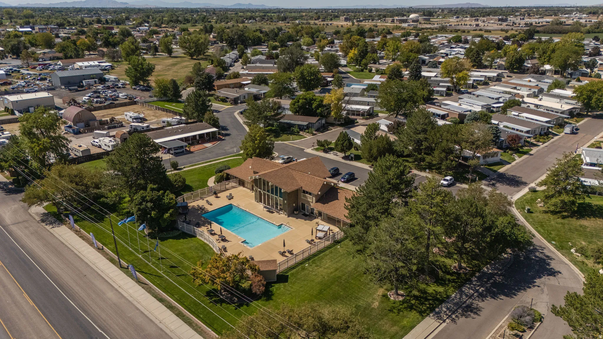 Community building with a large outdoor pool, concrete pool deck, and surrounding green space