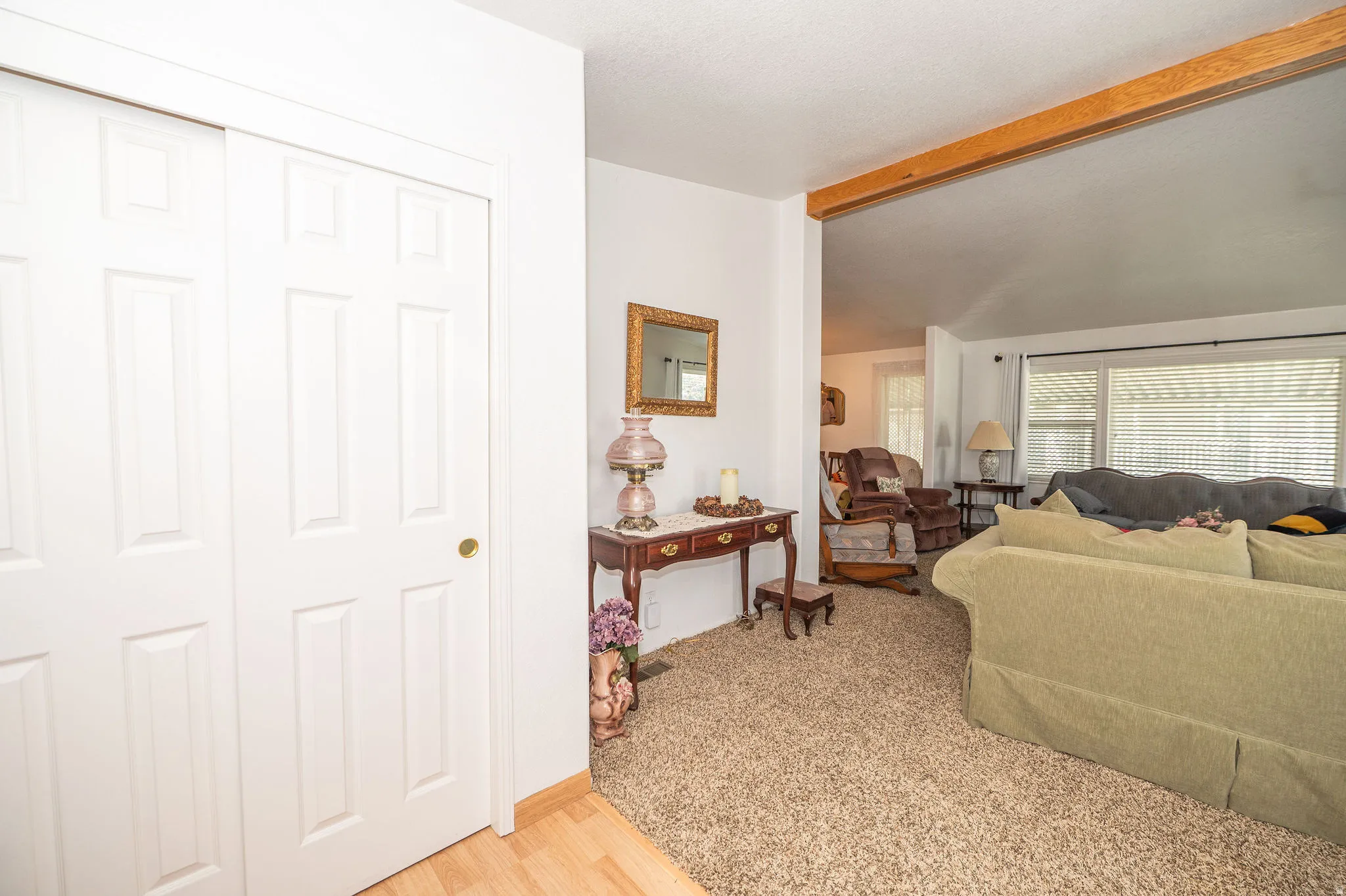 White panel doors, wood-finish flooring, exposed wood beam, carpeted living area, and window with blinds