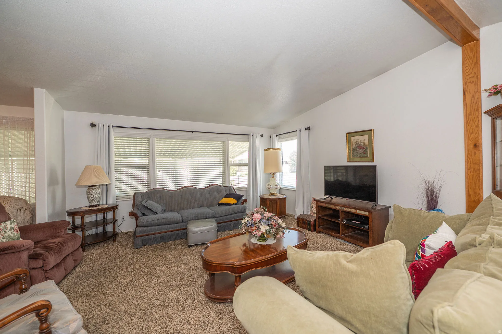 Spacious living area featuring expansive windows, wood-finish beam accent, and neutral-toned carpeting