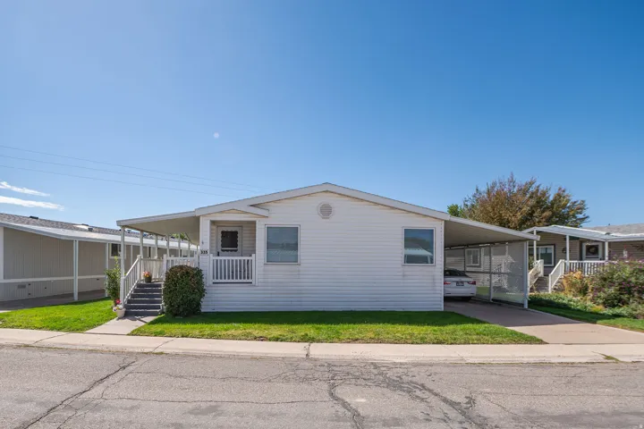 White siding exterior with a covered front porch, integrated carport, and a manicured lawn