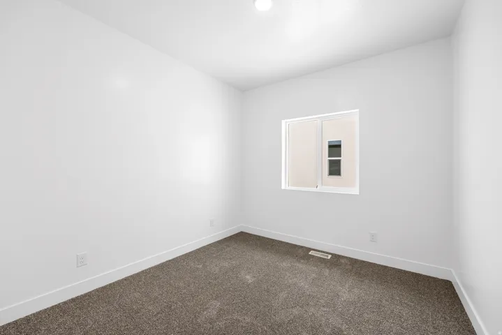 White painted walls with white trim, gray carpet flooring, and a single window