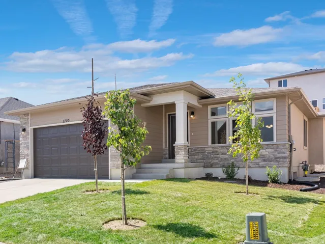Manicured lawn with mature landscaping, stone veneer siding, and an attached two-car garage
