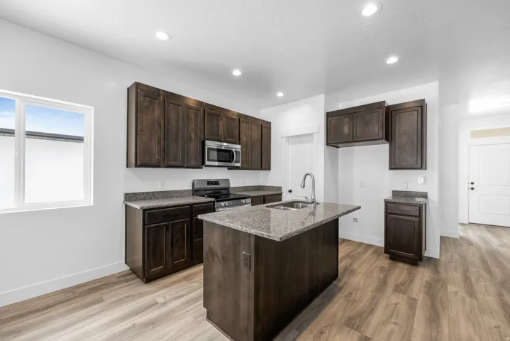 Kitchen featuring wood-finish flooring, dark wood cabinetry, light-toned countertops, a stainless steel range, and a stainless steel microwave