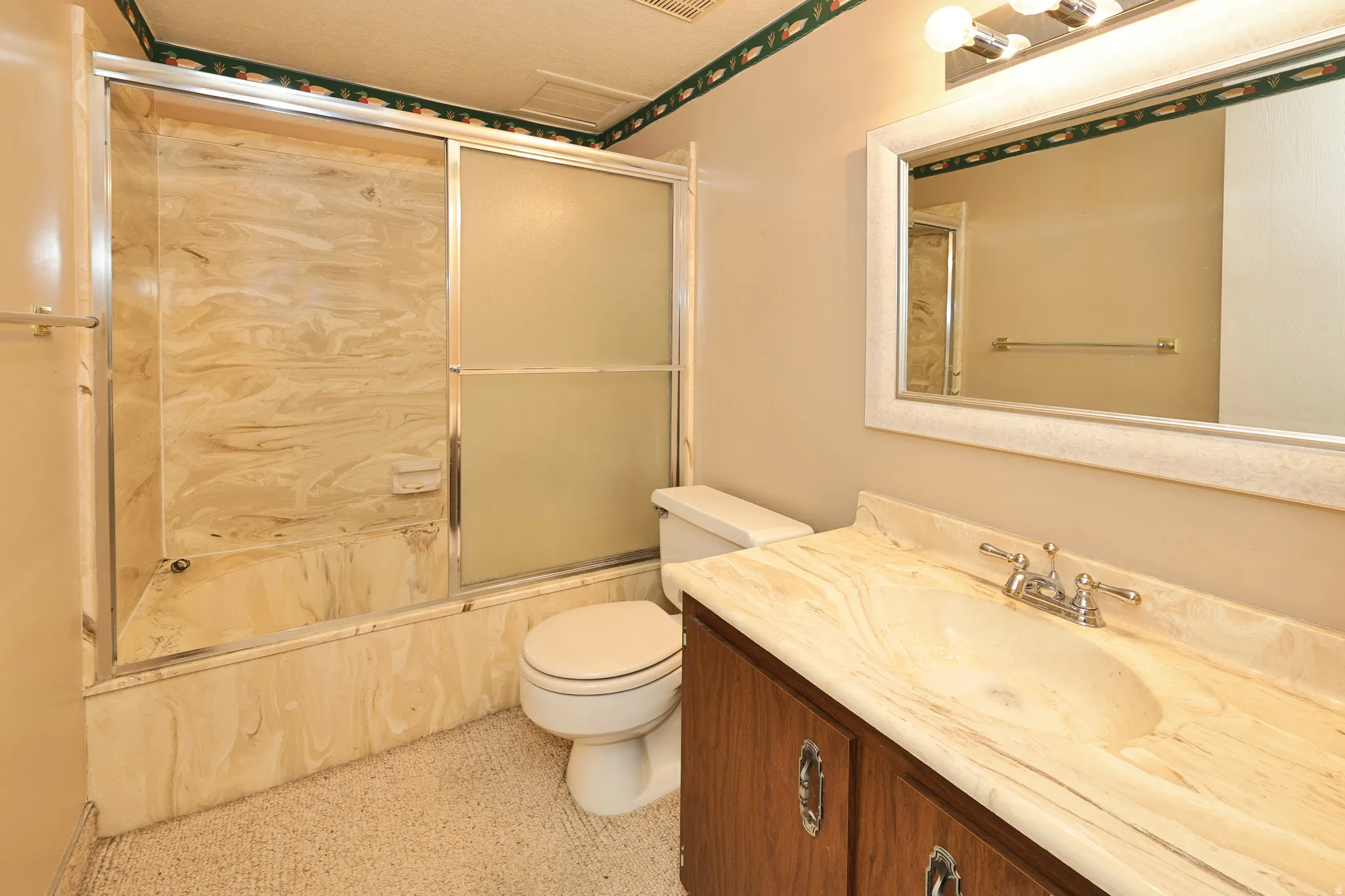 Bathroom featuring a built-in tub with sliding glass doors, a vanity with a light-toned countertop, and a framed mirror