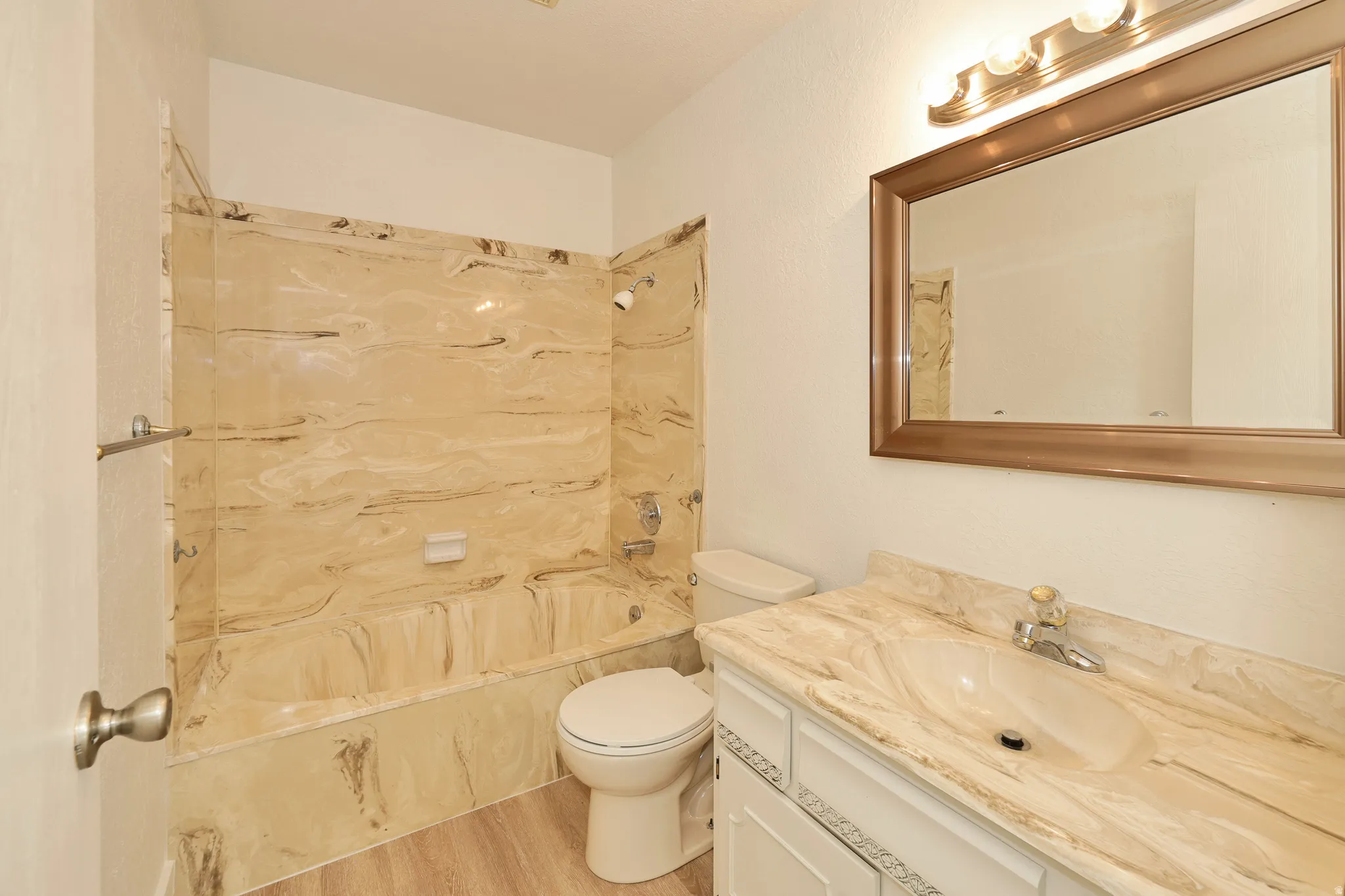Bathroom featuring a bathtub with a marble-look surround, a white vanity with a marble-look countertop and integrated sink, a framed mirror, and wood-finish flooring