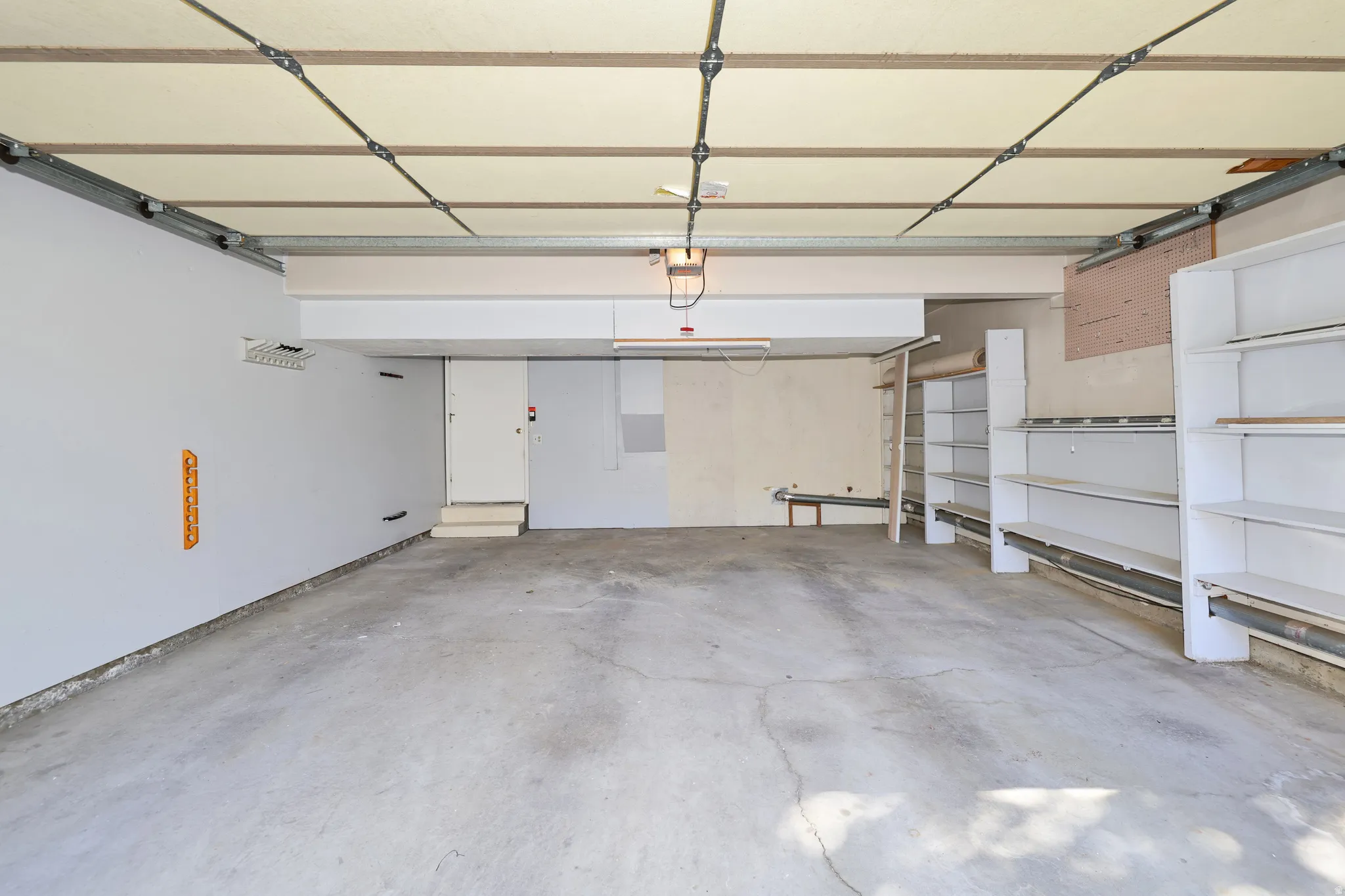 Spacious garage with concrete flooring, integrated shelving units, and a functional entry door
