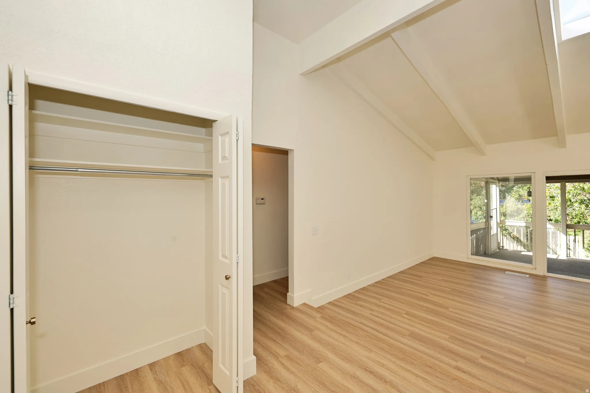 Vaulted ceiling with exposed beams, wood-finish flooring, and sliding glass doors to outdoor deck