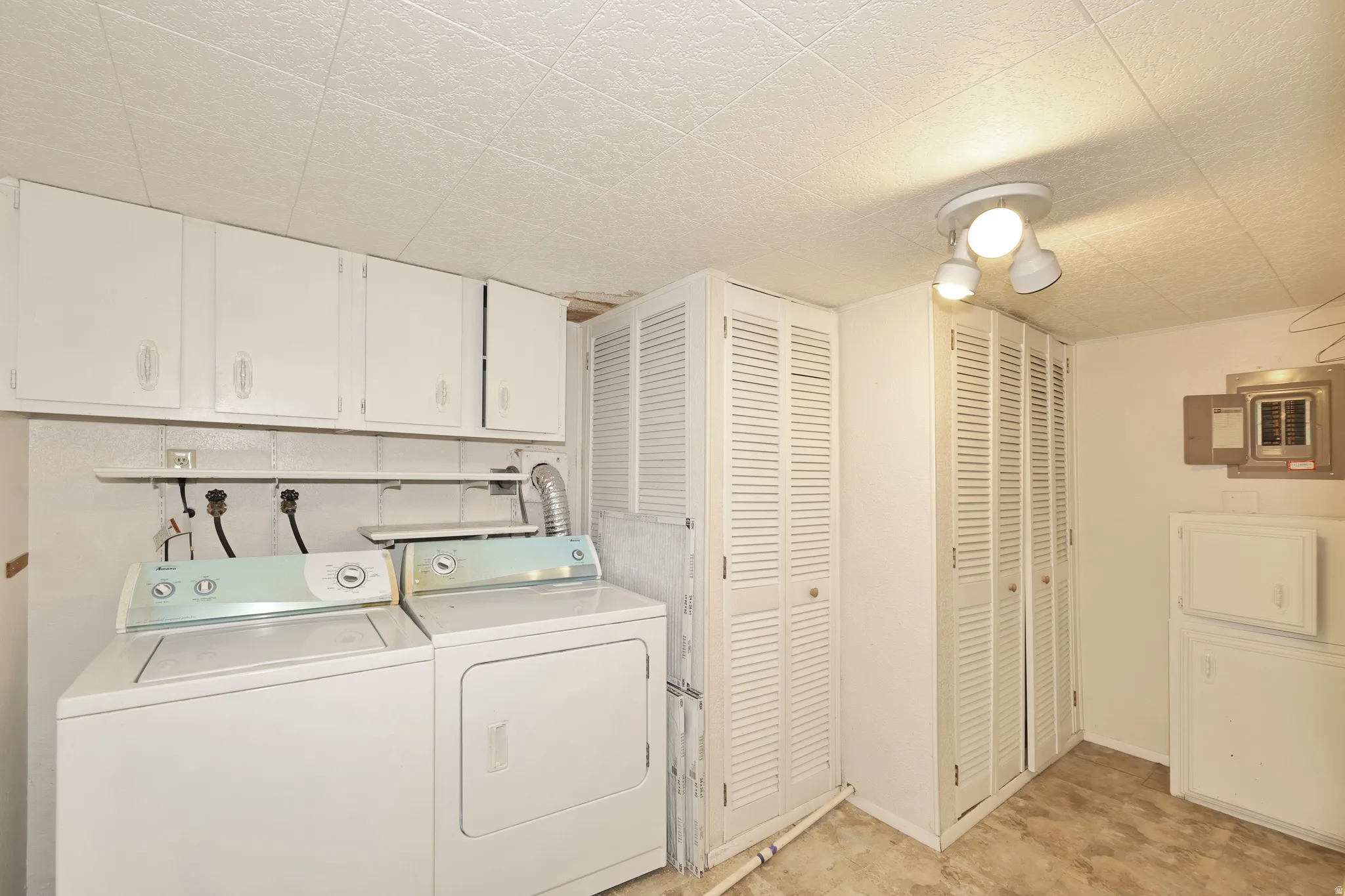 White upper cabinetry, built-in shelving, two louvered storage closets, flush-mount ceiling light fixture, and textured ceiling