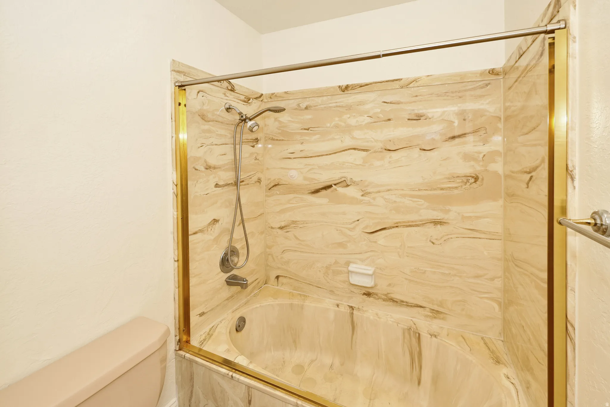 Bathtub with a shower fixture, integrated soap dish, and a gold-finish enclosure