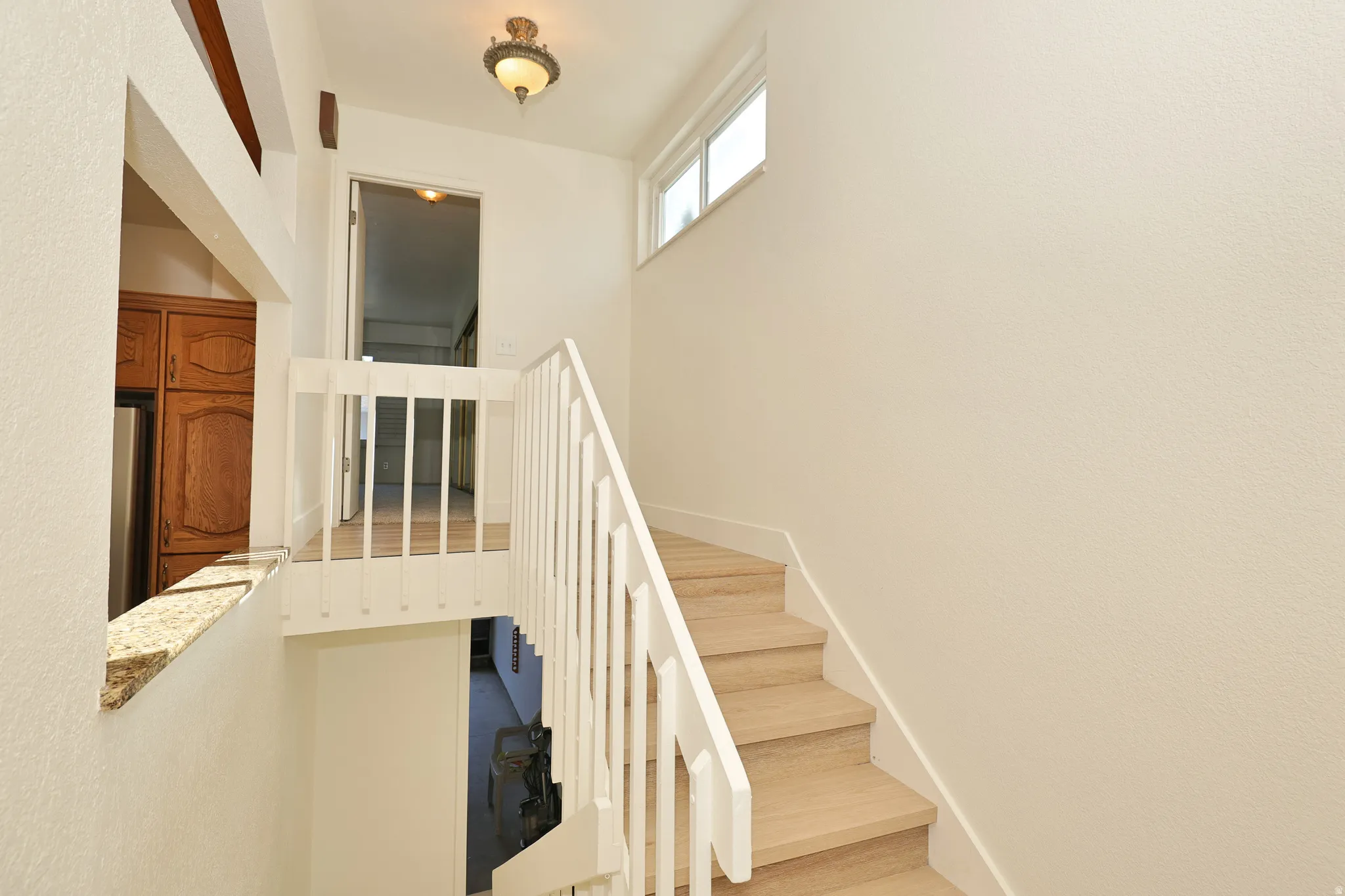 Light wood-finish staircase with white railings, upper floor landing with wood-finish flooring, and a wall-mounted light fixture