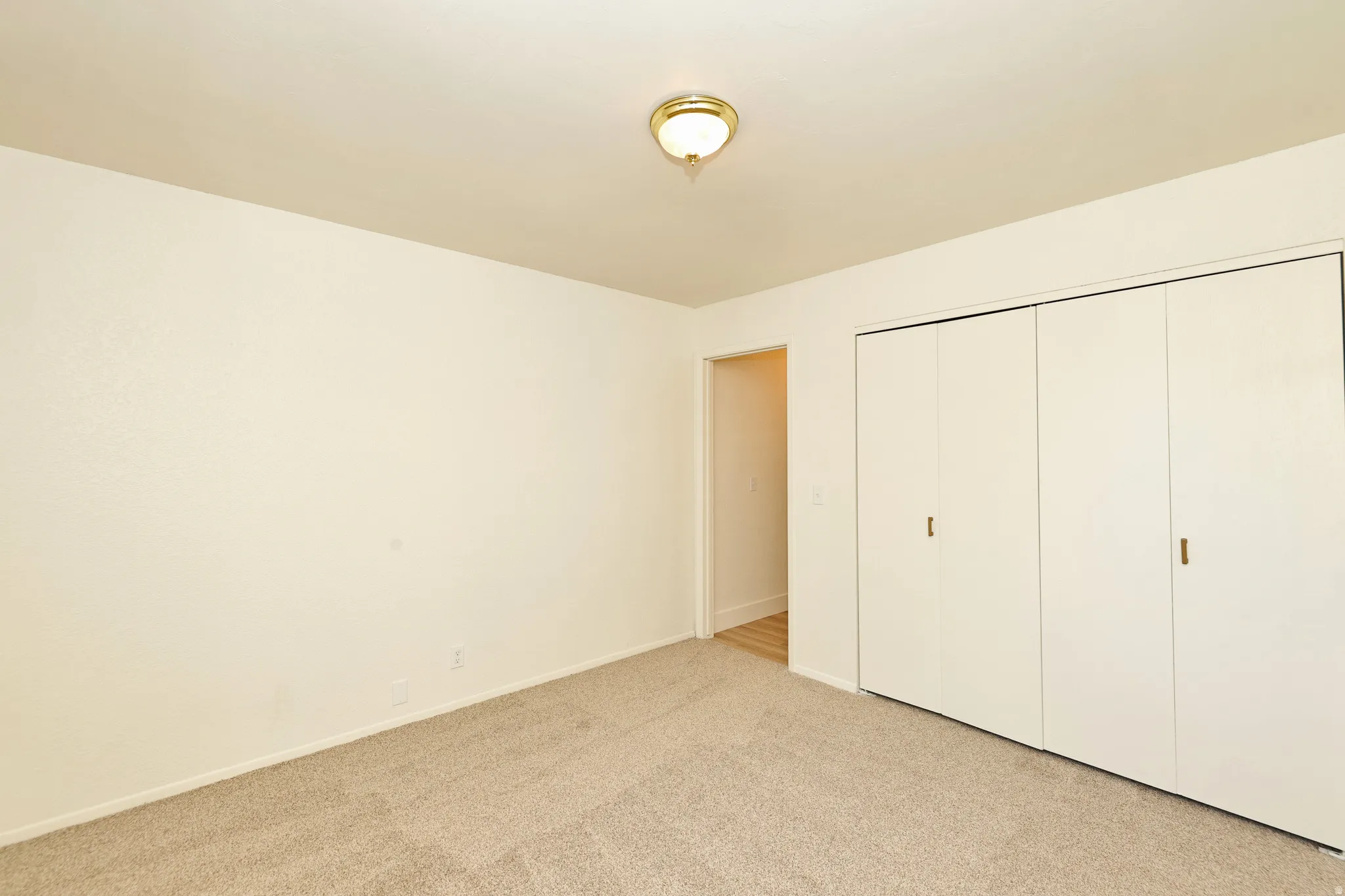 Light-colored textured walls, neutral carpeting, and a built-in closet with bi-fold doors