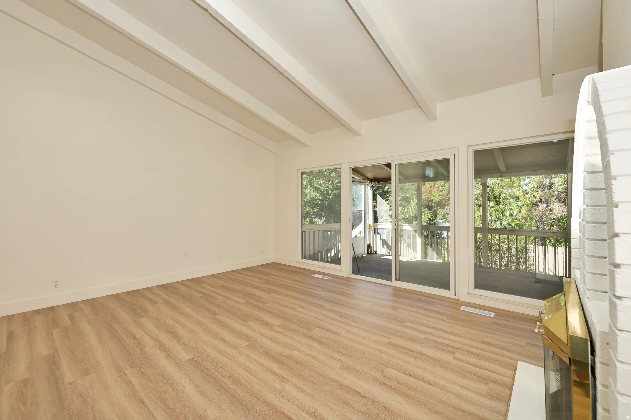 Spacious room featuring exposed ceiling beams, wood-finish flooring, and multiple sliding glass doors