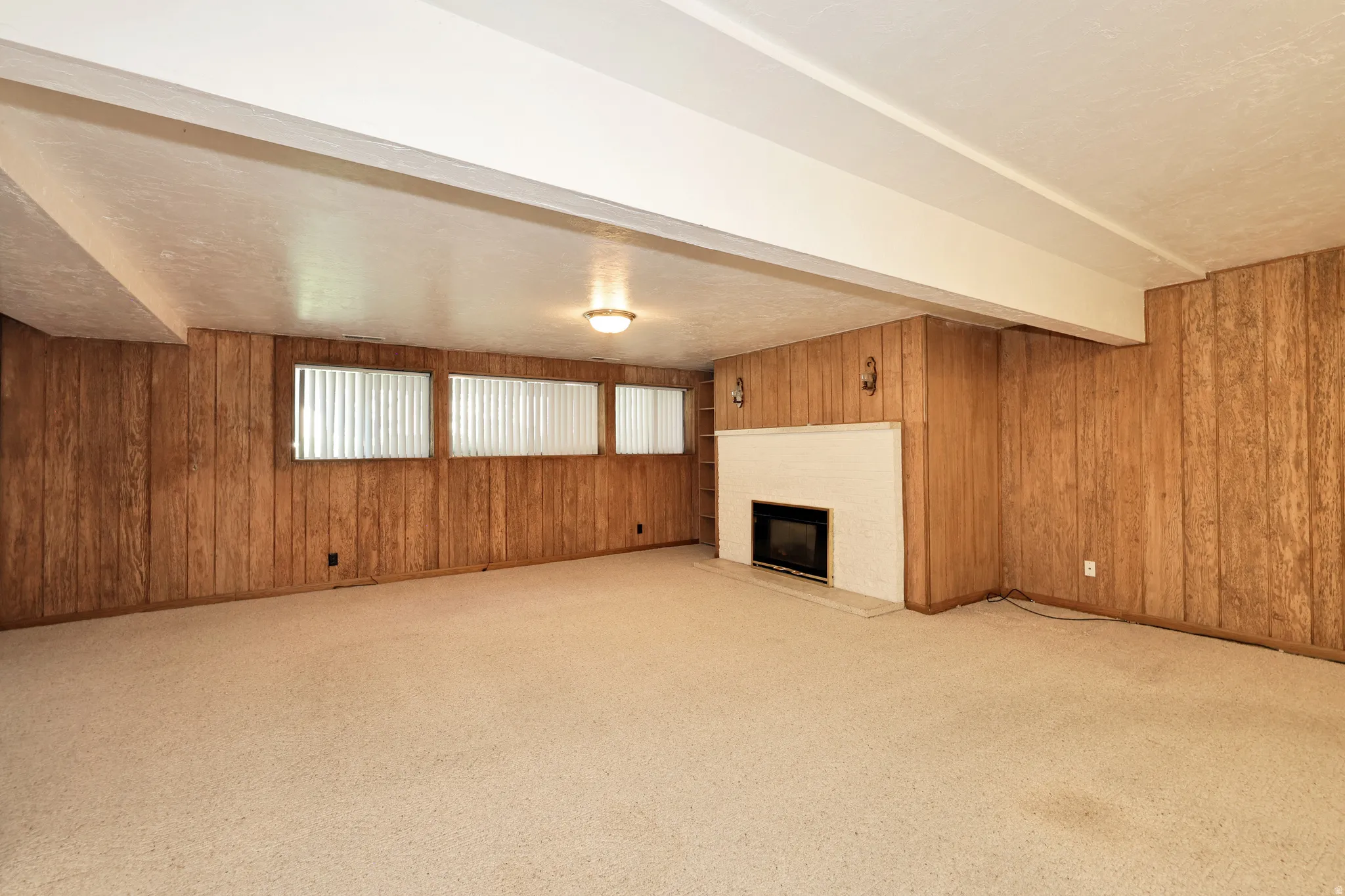 Expansive room with wall paneling, a fireplace with a white brick surround, and carpet flooring