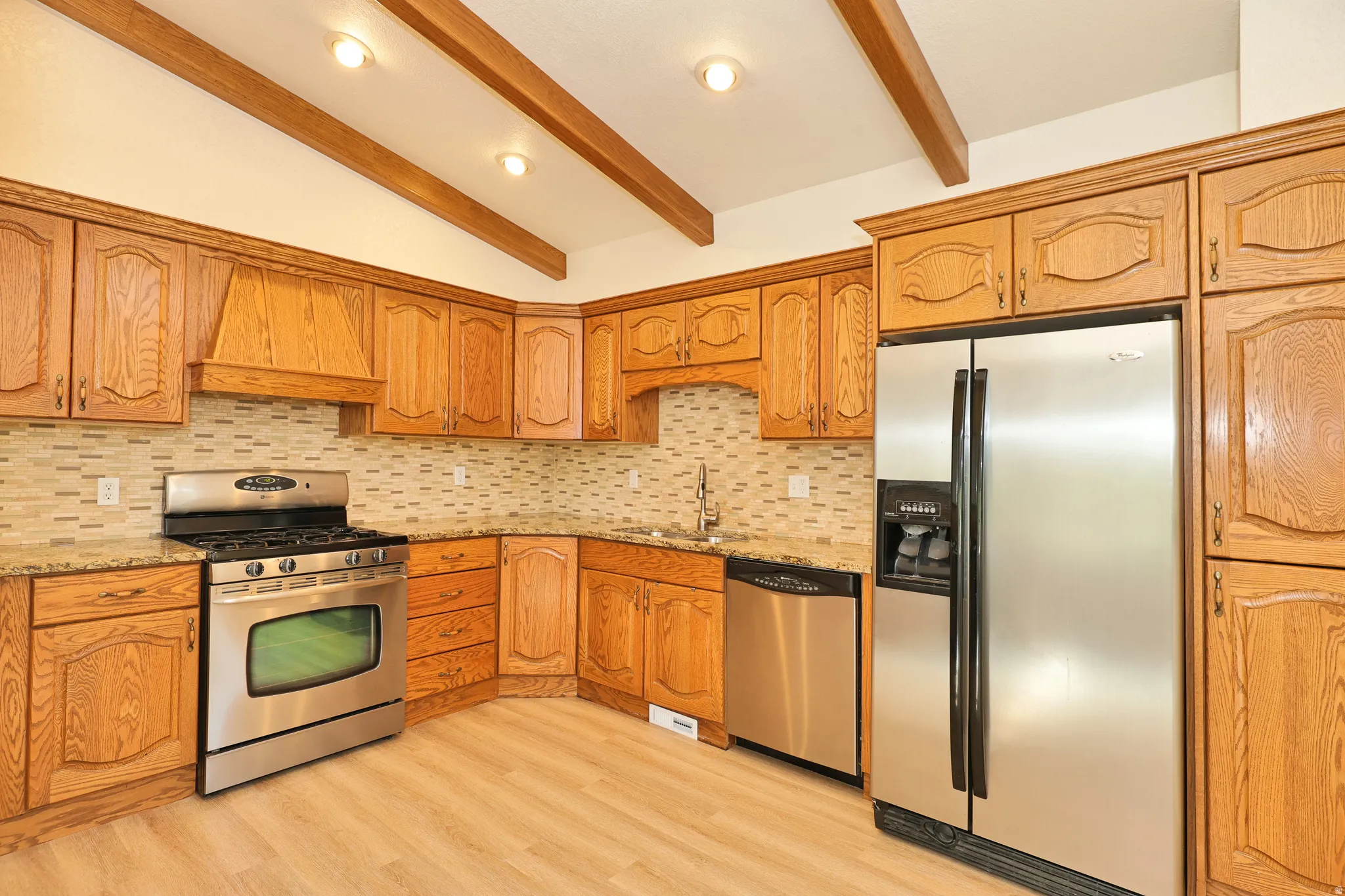 Kitchen featuring wood cabinetry, stainless steel appliances, mosaic tile backsplash, and wood-finish flooring