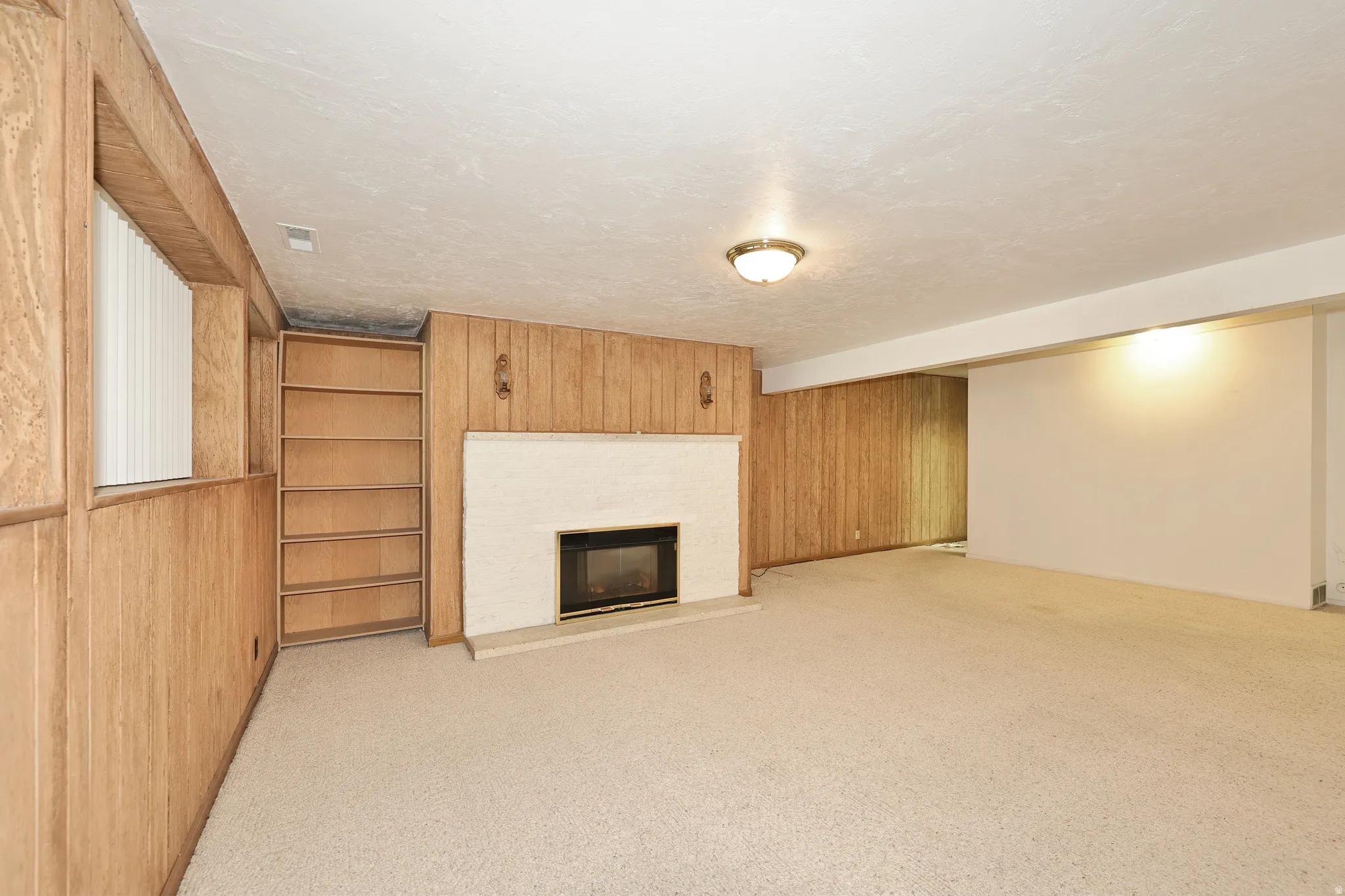 Carpeted room with a fireplace, built-in shelving, wood paneling, and a flush mount light fixture