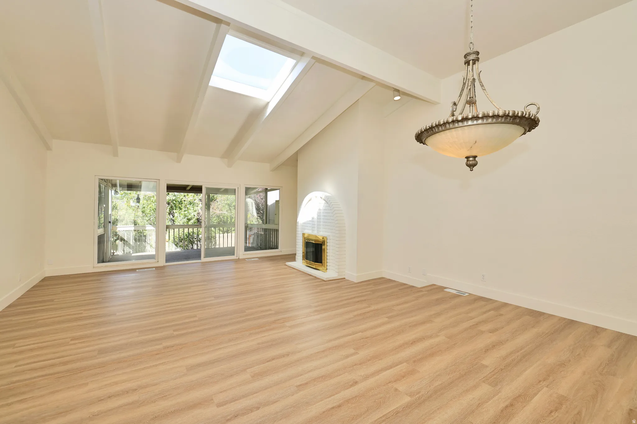 Vaulted ceiling with exposed beams, wood-finish flooring, skylight, and a built-in fireplace with a white brick surround