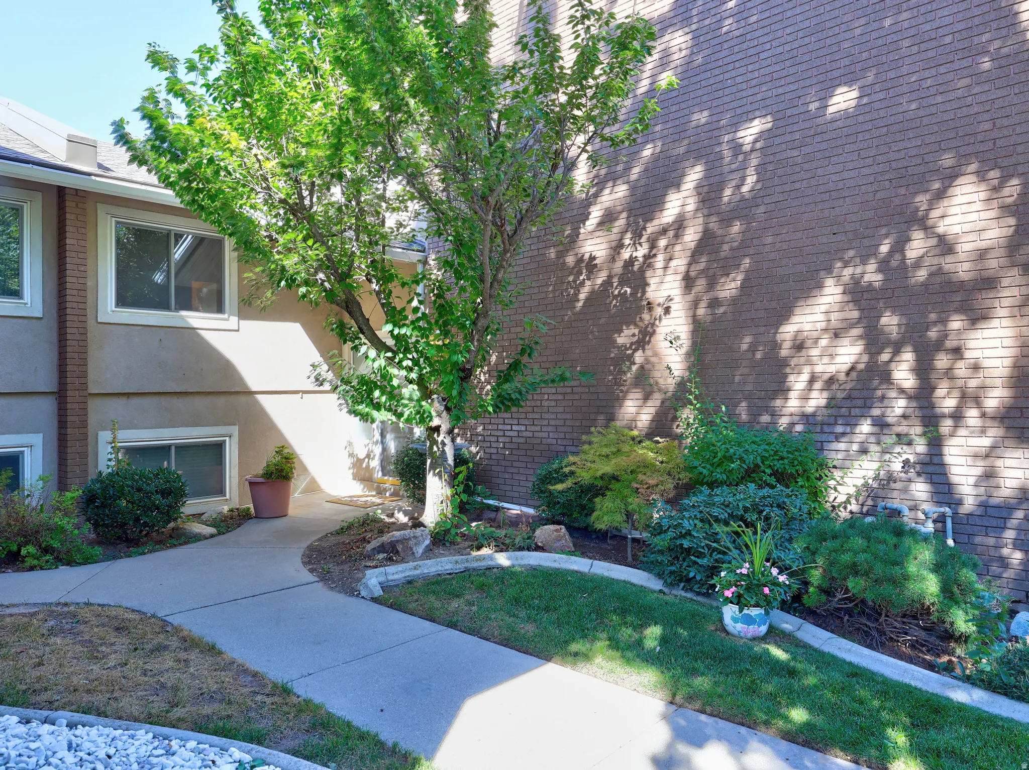 Manicured landscaping with mature trees, brick exterior, and a concrete pathway