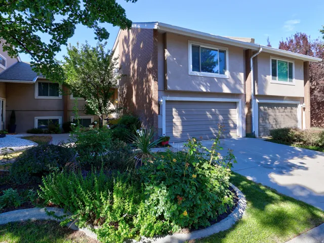 Stucco exterior with brick accents, attached garage, concrete driveway, front landscaping, and mature trees