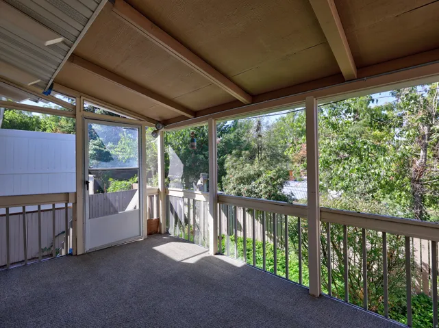 Screened patio with a carpeted floor, wood railings, and a solid overhead covering