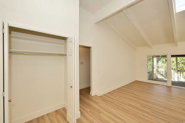 Vaulted ceiling with exposed beams, wood-finish flooring, and sliding glass doors to outdoor deck