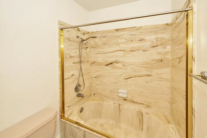 Bathtub with a shower fixture, integrated soap dish, and a gold-finish enclosure