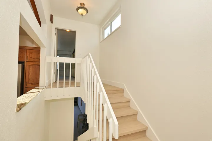 Light wood-finish staircase with white railings, upper floor landing with wood-finish flooring, and a wall-mounted light fixture