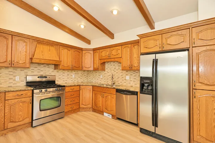 Kitchen featuring wood cabinetry, stainless steel appliances, mosaic tile backsplash, and wood-finish flooring