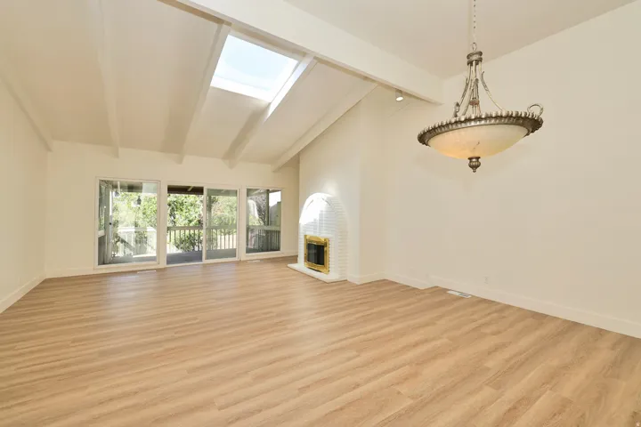 Vaulted ceiling with exposed beams, wood-finish flooring, skylight, and a built-in fireplace with a white brick surround