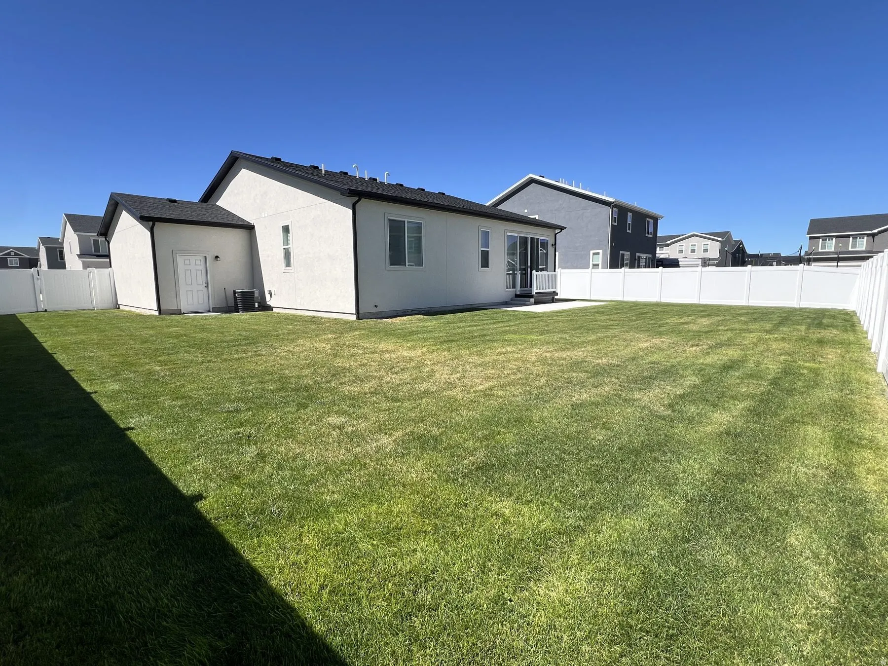 Expansive outdoor space featuring a manicured lawn, a white privacy fence, and a concrete patio