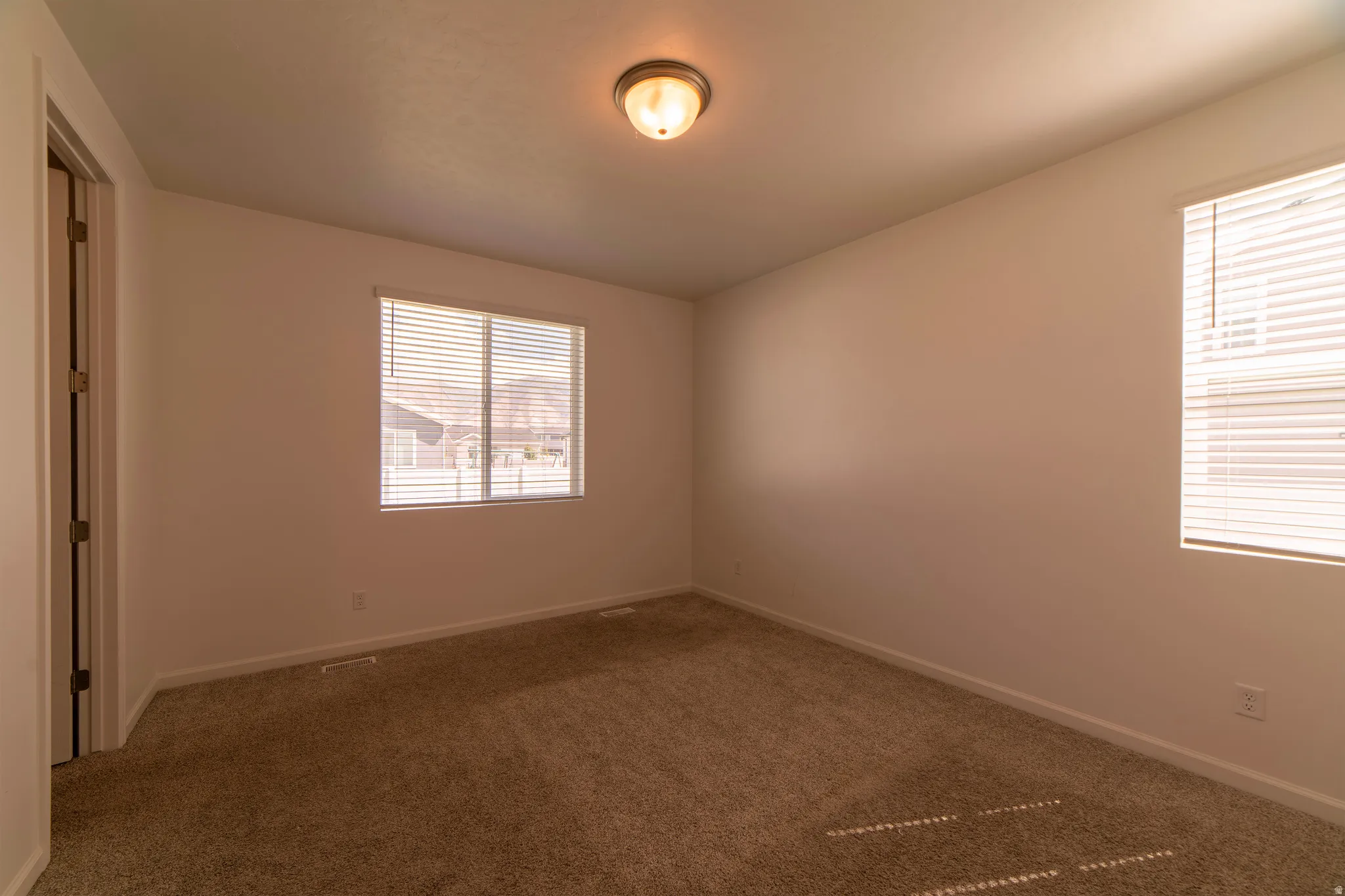 Neutral tone wall finishes, two windows with blinds, flush mount ceiling light, and wall-to-wall carpeting