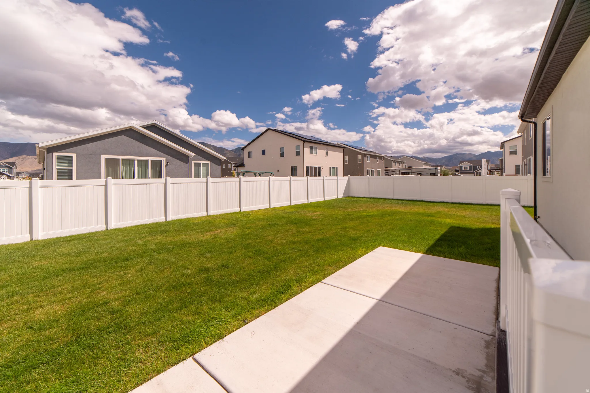Expansive backyard featuring a manicured lawn, full perimeter fencing, and concrete patio