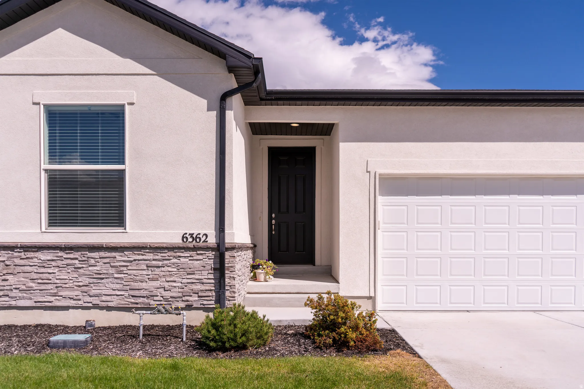 Stucco exterior with a stacked stone accent, dark front door, and an attached garage