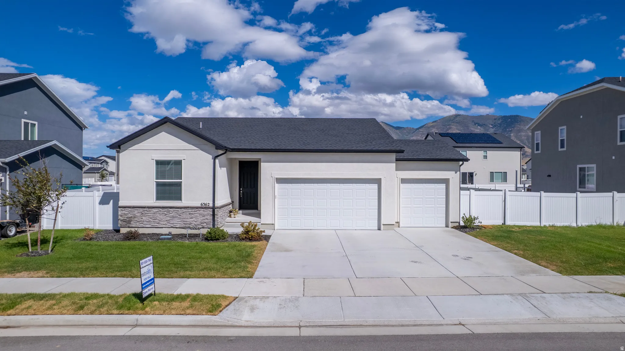 Contemporary single-story residence with a two-car garage, partial stone façade, and a dark shingle roof
