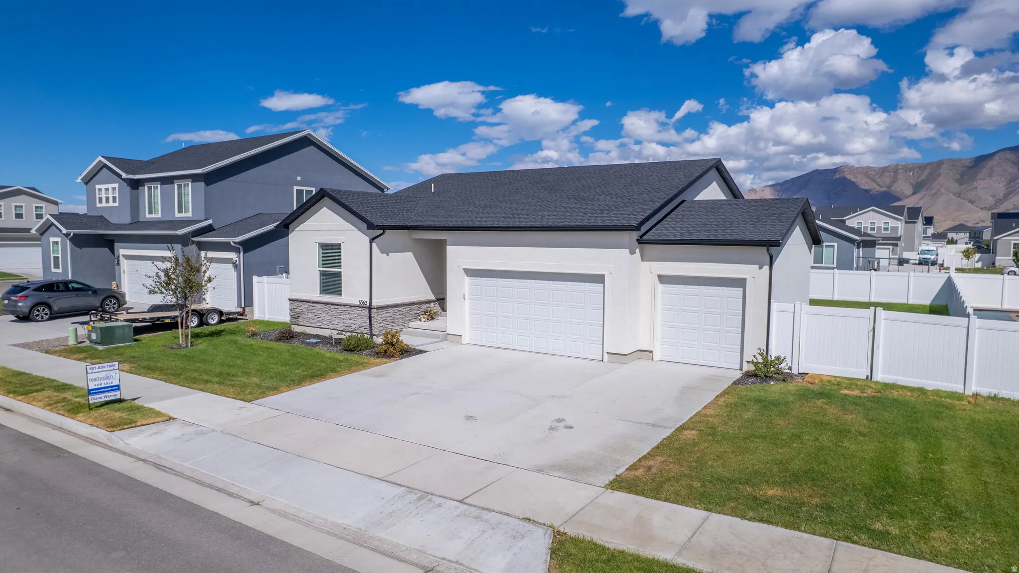 Contemporary exterior with white stucco and stone accents, dual garage doors, and a paved driveway