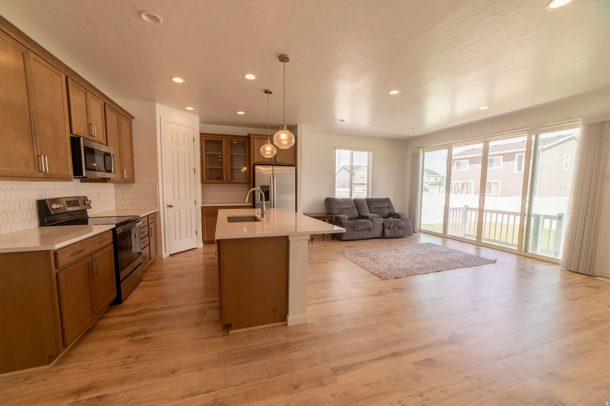 Open-concept living space with wood-finish flooring, recessed lighting, and a kitchen island featuring pendant lighting