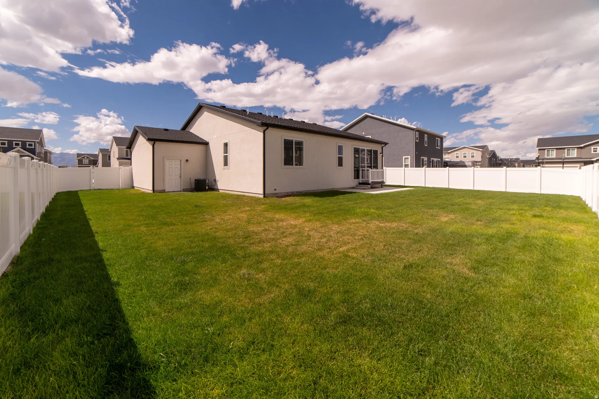 Expansive backyard with a manicured lawn, full vinyl privacy fencing, and a white exterior home with black-framed windows