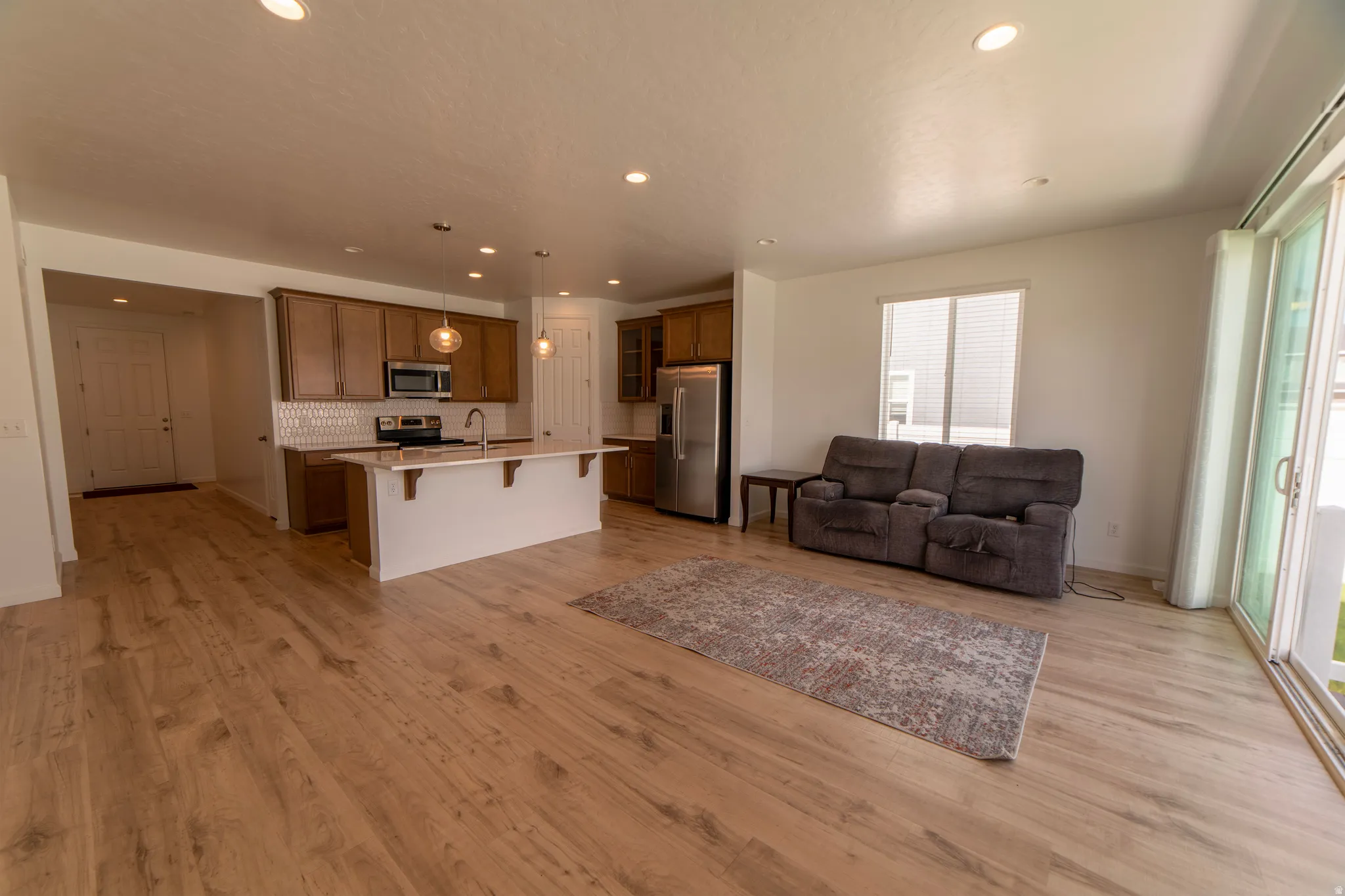 Open-concept living space with wood-finish flooring, recessed lighting, and a kitchen island with pendant lighting